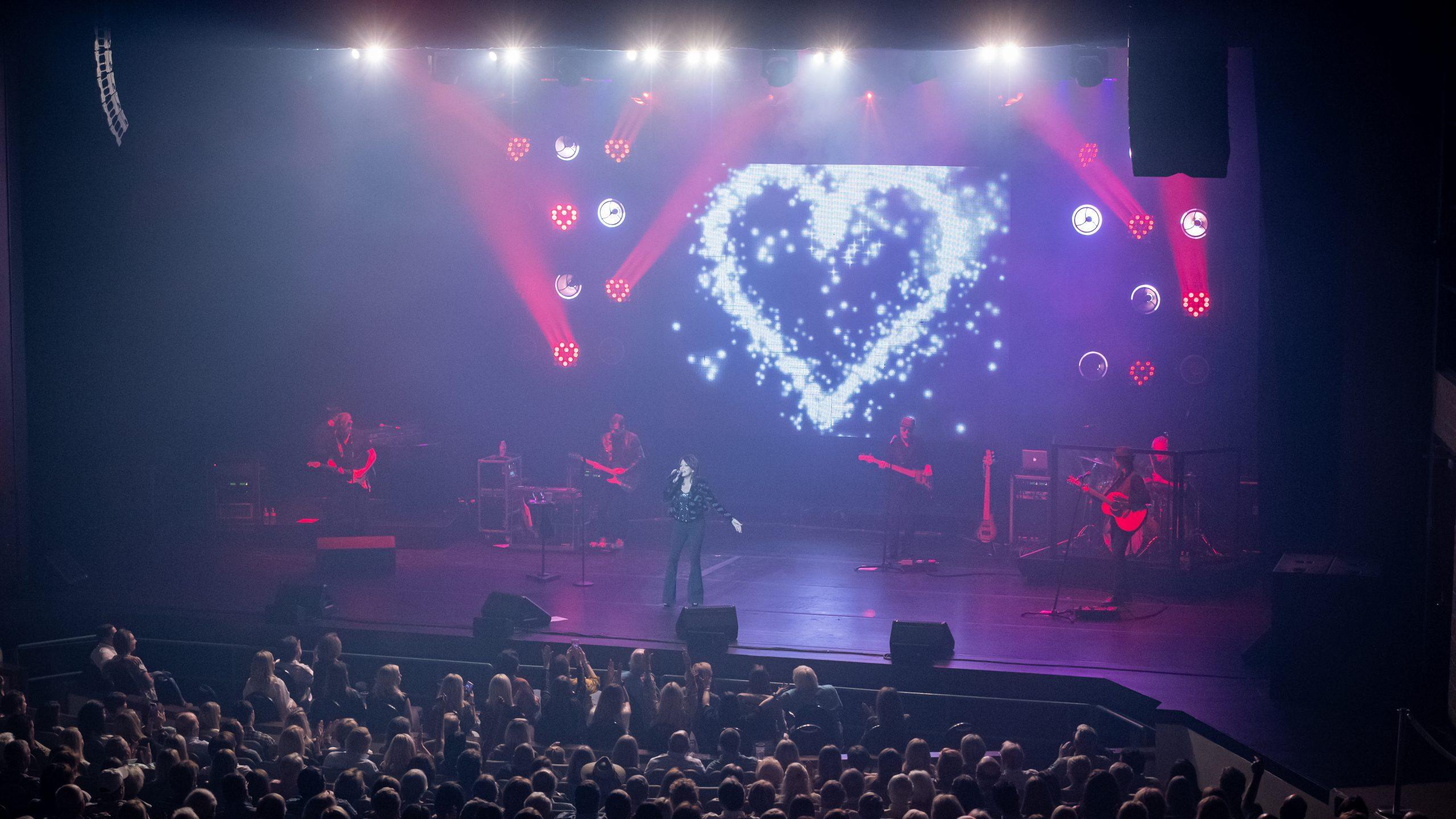 A band performing at a live concert with lights and large crowd at 博洛尼亚表演艺术中心.